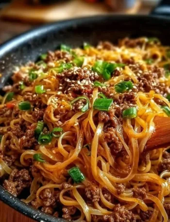 Plate of Mongolian ground beef noodles topped with green onions and sesame seeds.