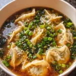 A bowl of potsticker soup garnished with fresh herbs and spices.