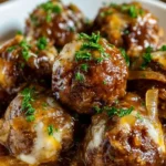 Crockpot French Onion Meatballs served on a plate with melted cheese and fresh herbs